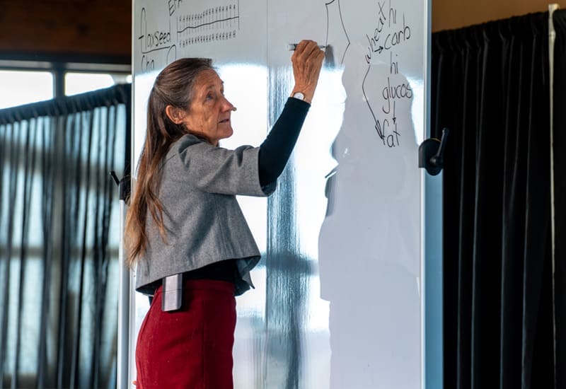 Barbara O'Neill in front of whiteboard making notes for those in attendance